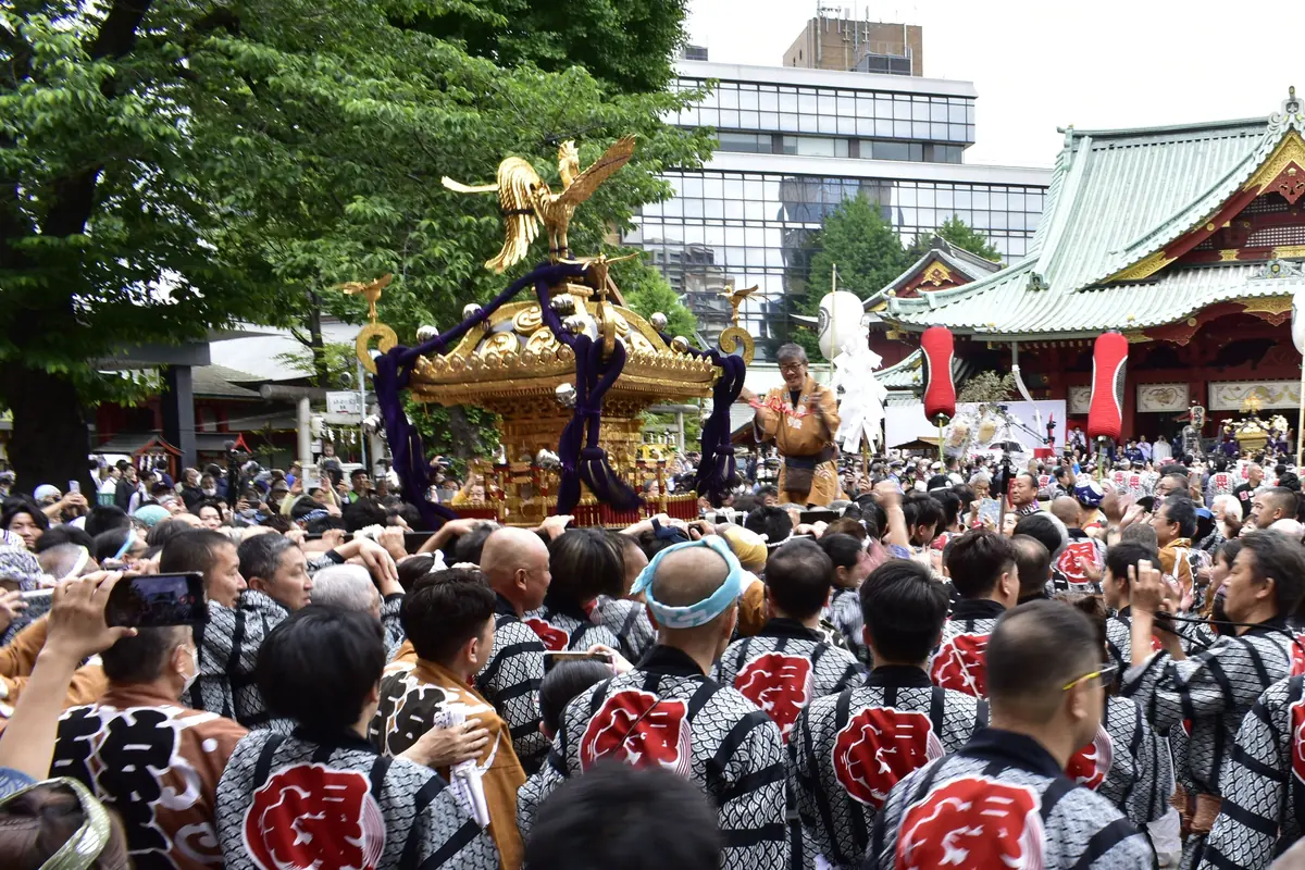 A gilded portable shrine carried by a crowd in festival coats outside the main hall of Kanda Myojin during the Kanda Matsuri