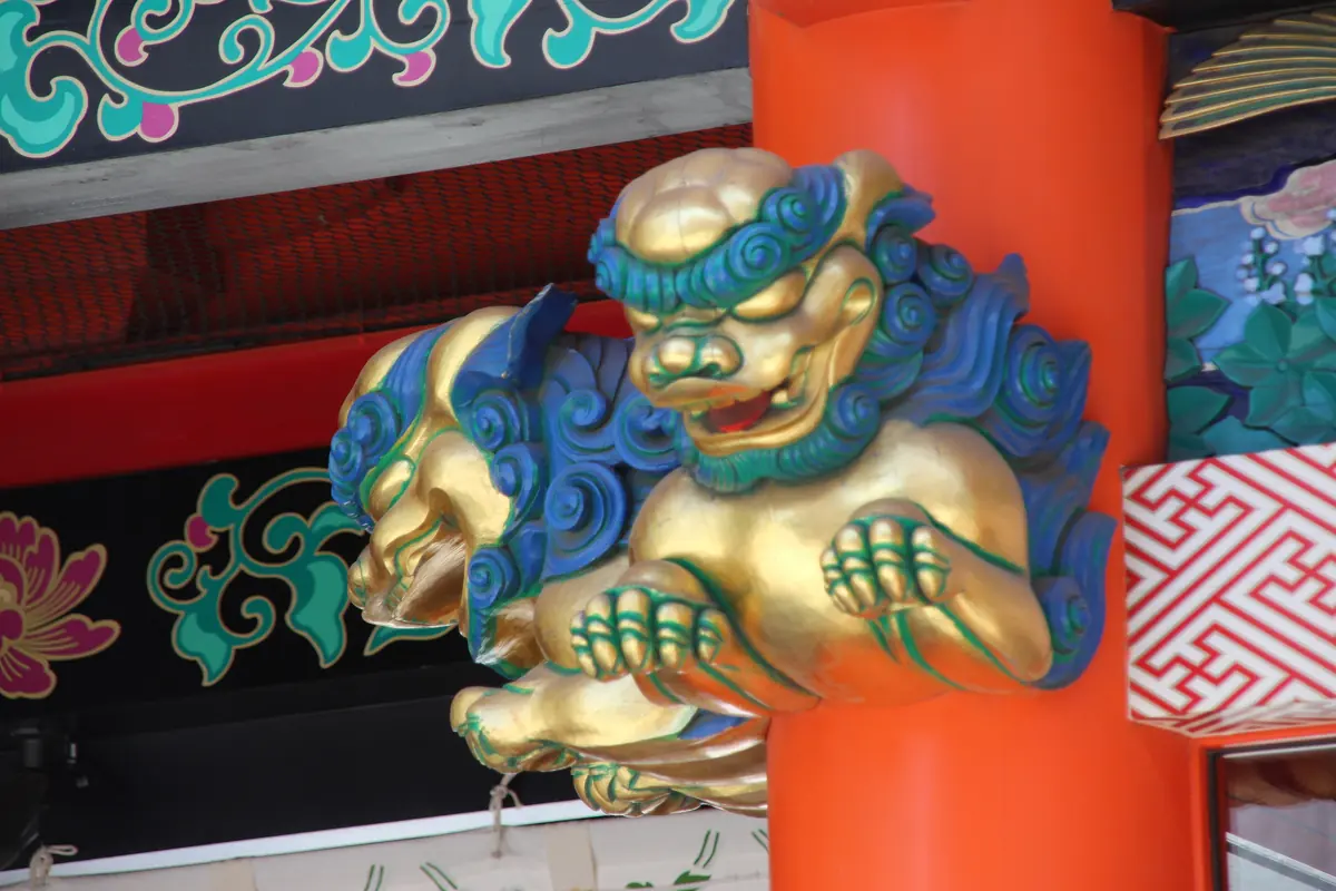 A gilded and blue carved lion-like beast on a vermilion pillar beneath painted beams at Kanda Myojin shrine