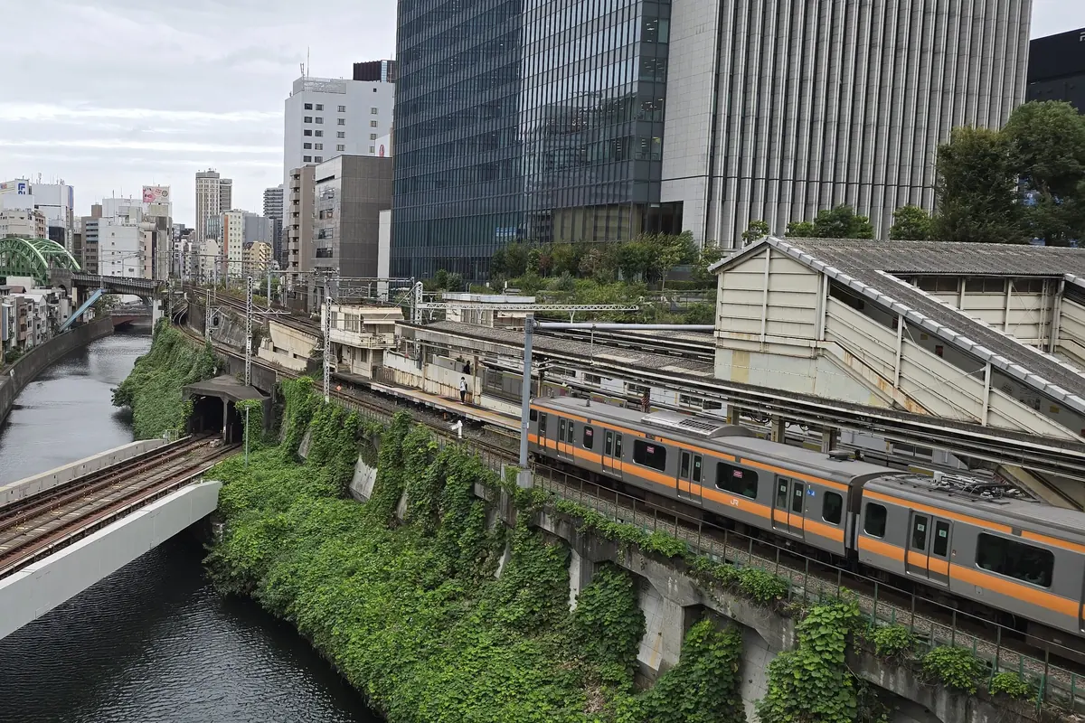 An orange-striped commuter train running beside the Kanda River in Tokyo, with office towers beyond